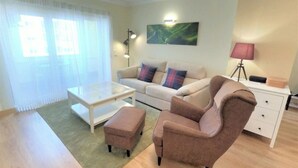A living room with a sofa, armchair, ottoman, coffee table, and a lamp. - Carnaxide, modern T1 apartment w/ balcony, Lisbon (Carnaxide)