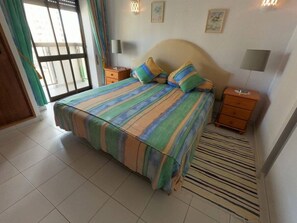 Quarto com cama, duas mesas de cabeceira, janela com cortinas e luminária na parede.