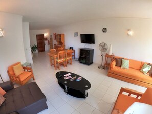 Uma sala de estar com sofá, poltrona, mesa de centro, televisão e um espaço de jantar com cadeiras e mesa.