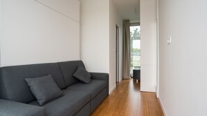 Una sala de estar moderna con un sofá gris, piso de madera y vistas a un balcón.