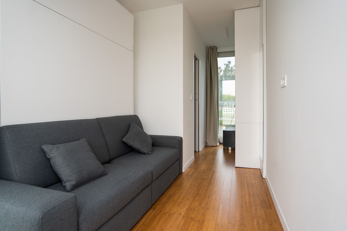 A modern living room with a grey sofa, wooden flooring, and a view to a balcony.