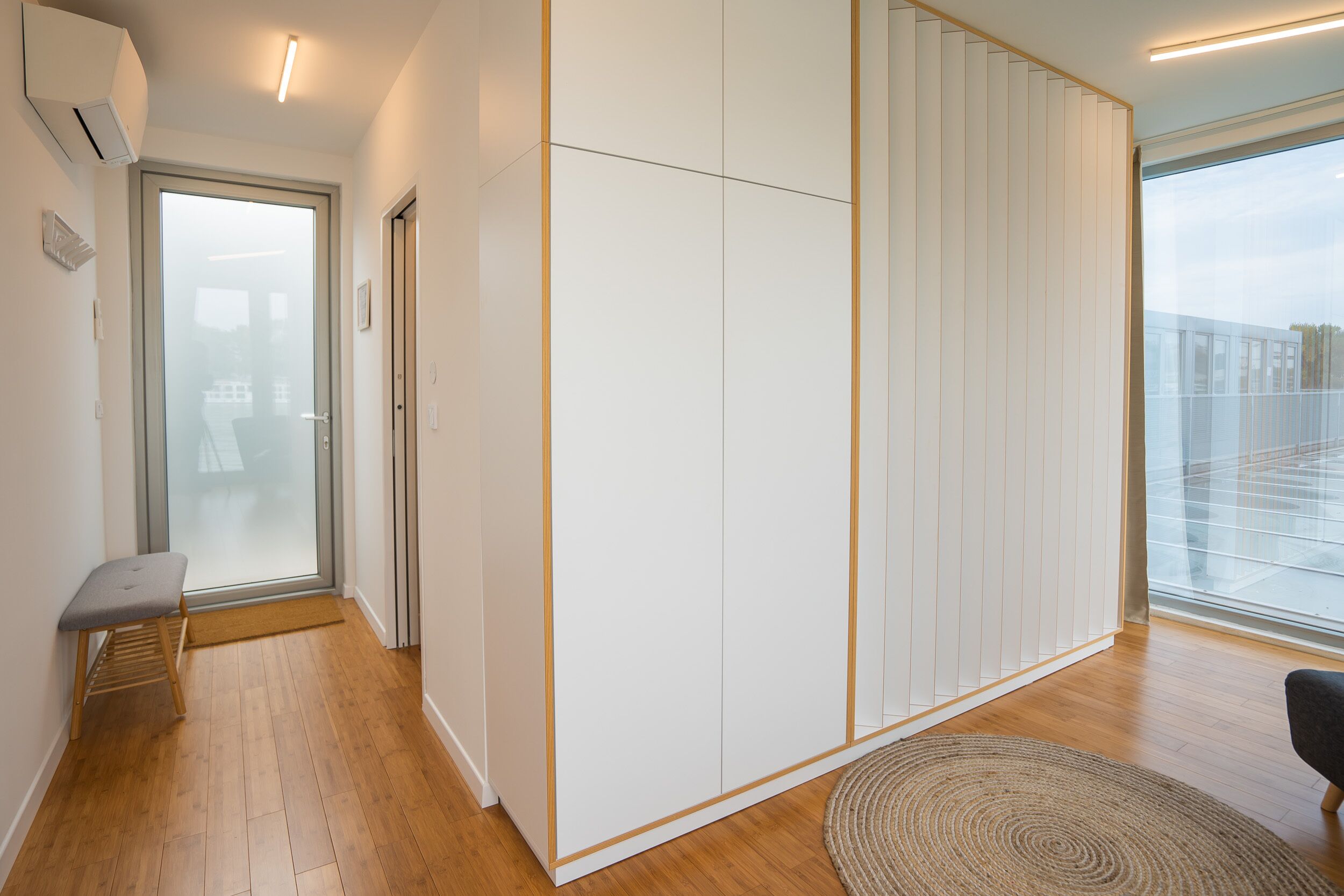 A modern room with a sliding door, a bench, a large window, and a wooden floor.