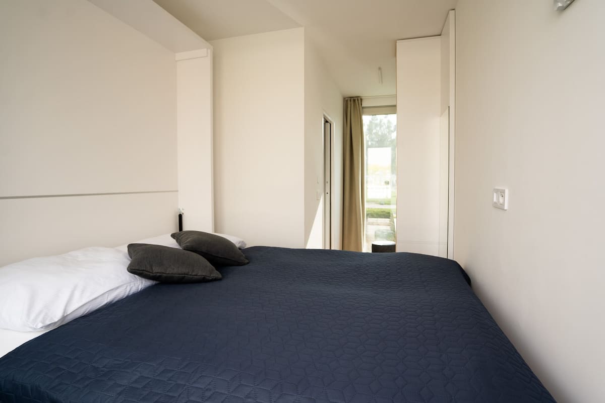 A bedroom with a large bed, a window with curtains, and a door leading to an outdoor area.