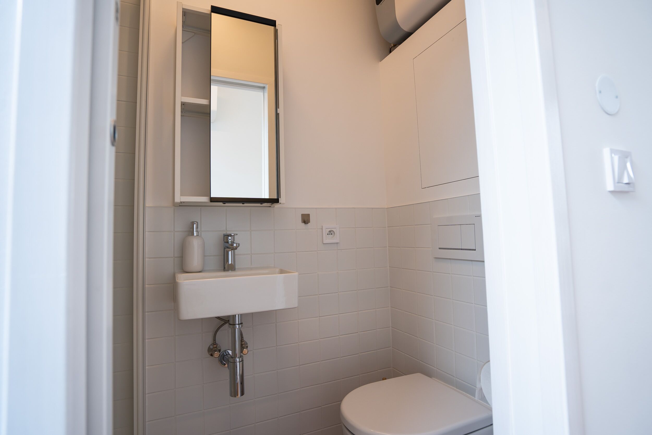 A small, modern bathroom with a white sink, mirror, and toilet.