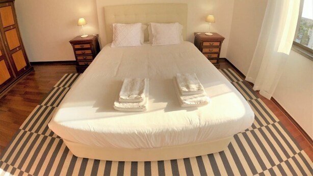 A hotel room with a large bed, two bedside tables, a chandelier, and a window with curtains. - Lisbon, T2 apartment in condominium, Linda-a-Velha (Linda a Velha)