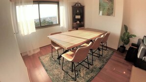 A dining room with a large table, chairs, a cabinet, a potted plant, and a view through a window. - Lisbon, T2 apartment in condominium, Linda-a-Velha (Linda a Velha)