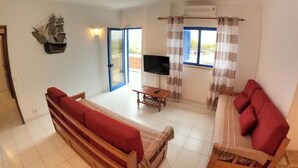 Una habitación amplia con una cama grande, televisión, una mesita y un balcón con cortinas.