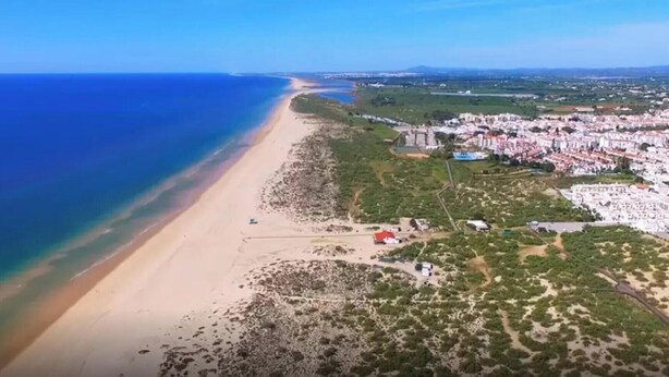 Vista aérea de una zona costera con playa, un pequeño poblado y una extensa masa de agua.