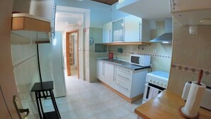 A compact kitchen with white cabinets, a microwave, a stove, and a small table. - Lisbon T2 apartment in typical villa, Sapadores (Lisboa ciudad)