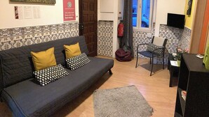A living room with a sofa, a chair, a small table, a TV, and a door leading outside. - Lisbon T2 apartment in typical villa, Sapadores (Lisboa ciudad)