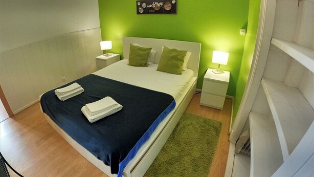 A neatly made bed with a blue blanket and pillows, two bedside lamps, a green wall, and a small artwork above the bed. - Lisbon T2 apartment in typical villa, Sapadores (Lisboa ciudad)