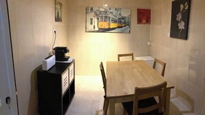 A dining area with a wooden table and chairs, a coffee machine, and a painting of a tram on the wall. - Lisbon T2 apartment in typical villa, Sapadores (Lisboa ciudad)