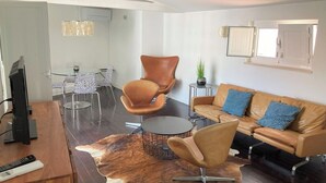 En moderne stue med en lædersofa, et rundt sofabord og et spiseområde med et glasbord og stole.