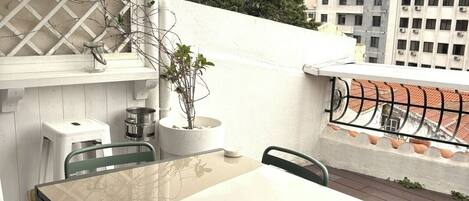 Terraza en la azotea con una mesa, sillas, una planta en maceta y vistas a edificios.
