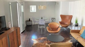 En moderne stue med et fladskærms-tv, lædersofaer og et spiseområde med et glasbord og stole.