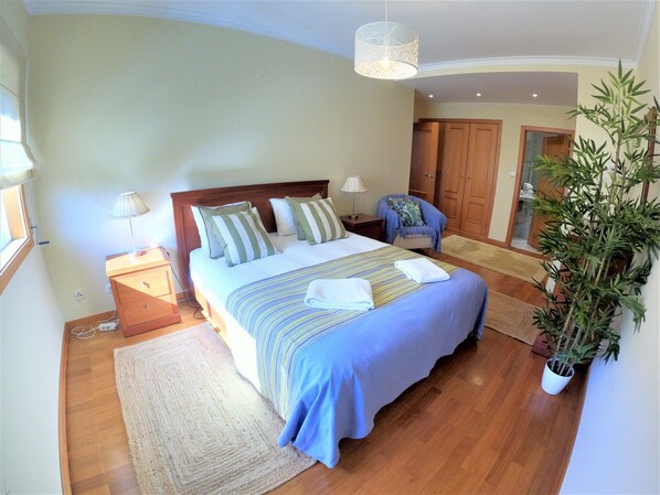Une chambre Ă coucher avec un lit, des tables de chevet, une chaise, une plante en pot et un plancher en bois.