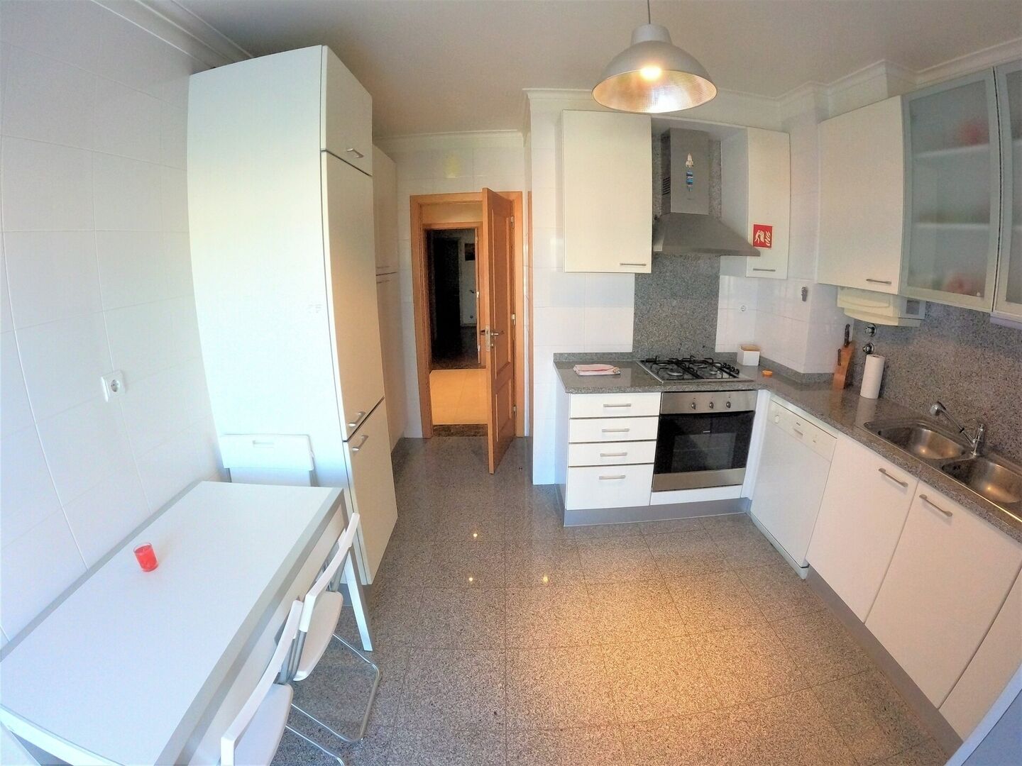 Une cuisine compacte avec des meubles blancs, une cuisinière à gaz, un four encastré et un évier.