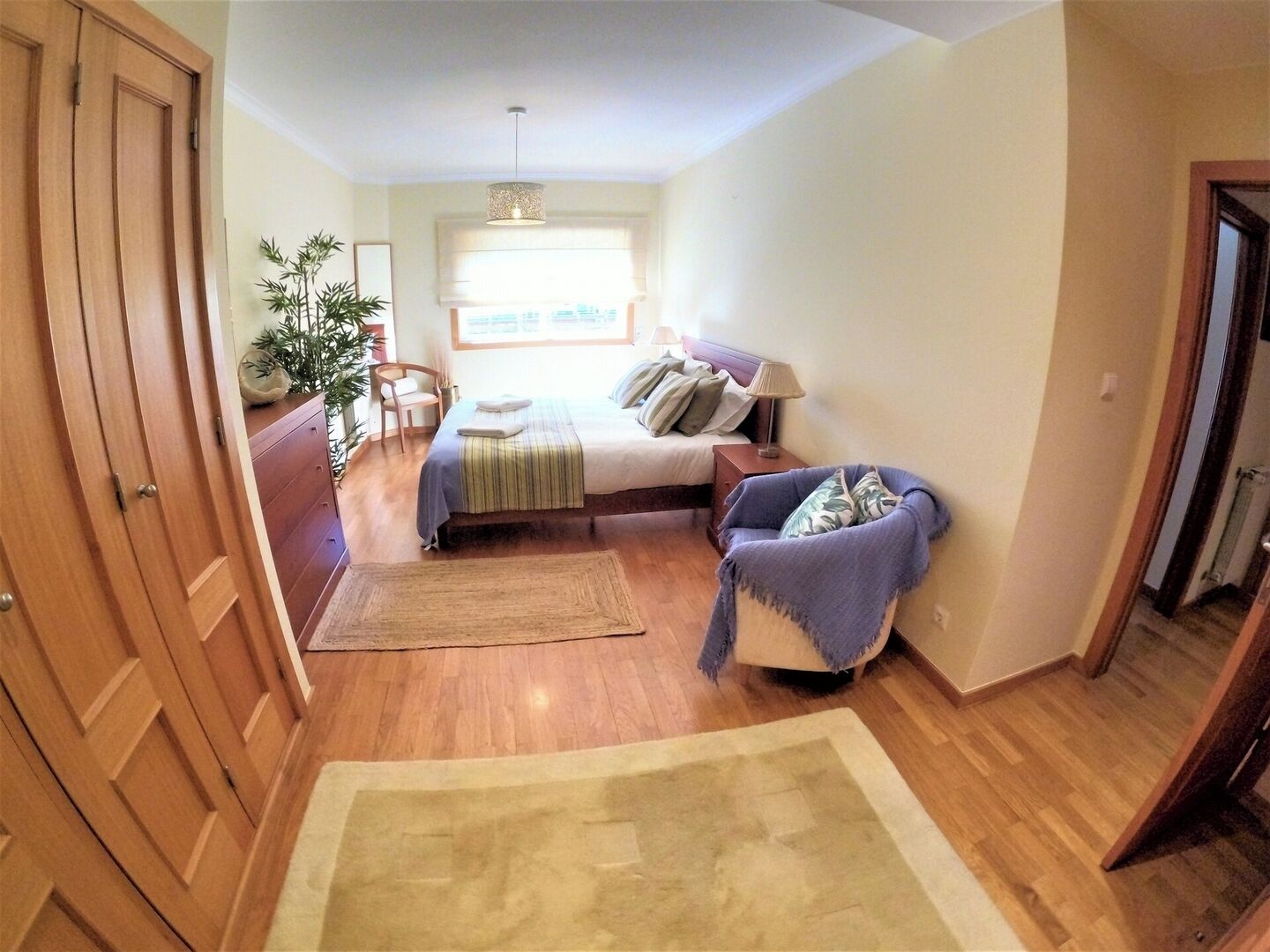 Quarto com cama, mesa de cabeceira, cadeira e vista para o exterior.