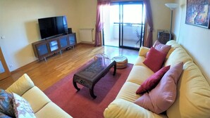 Een woonkamer met een bank, een salontafel, een televisie en een schuifdeur die leidt naar een balkon.