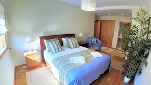 Een slaapkamer met een bed, nachtkastjes, een lamp, een stoel, een kamerplant en een kledingkast.