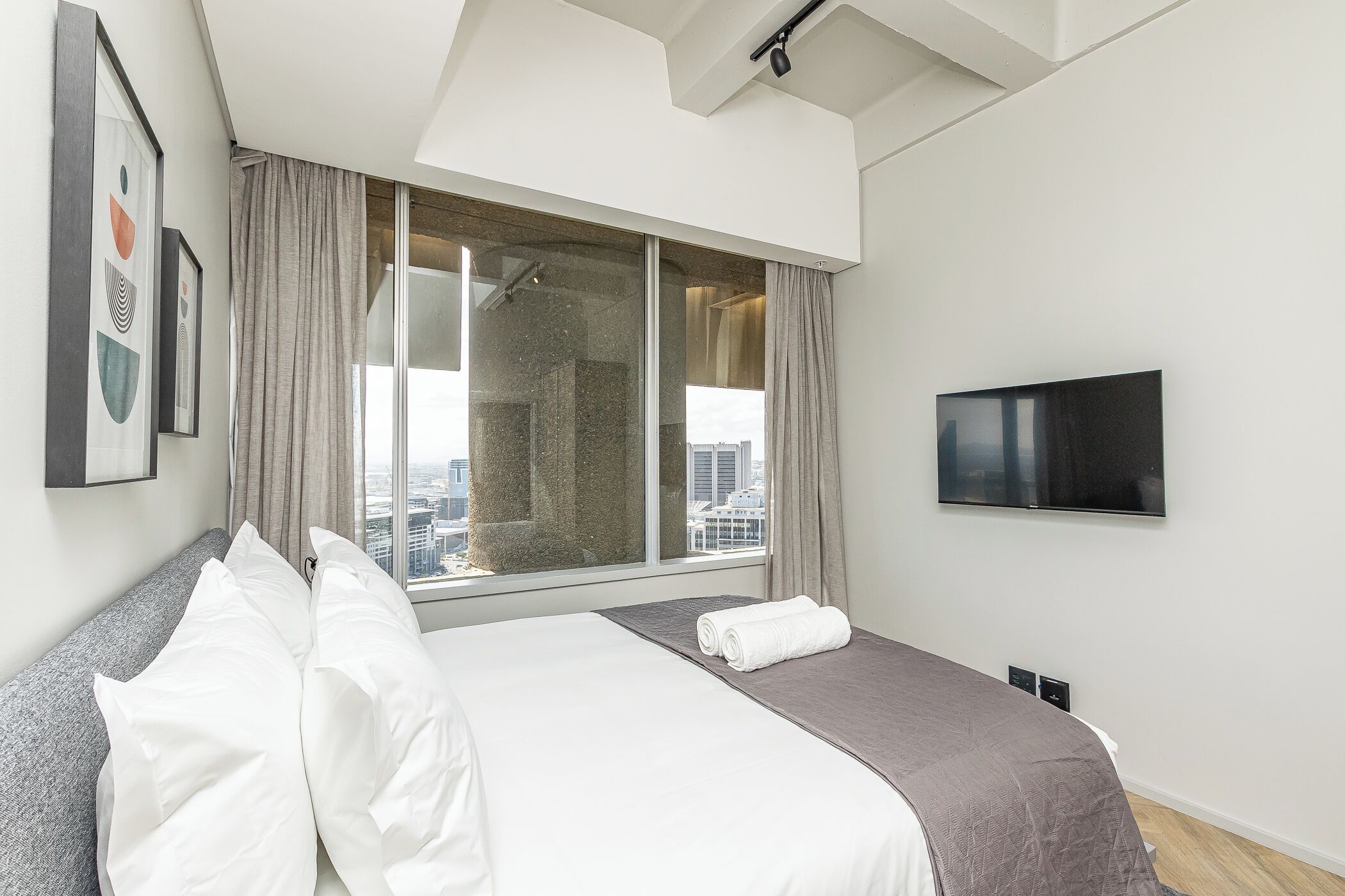 Une chambre d’hôtel moderne dotée d’un grand lit, d’un téléviseur à écran plat et offrant une vue sur la ville grâce à une grande fenêtre.