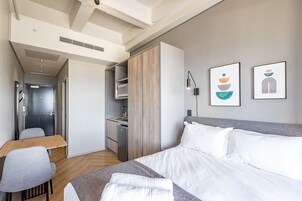 Une chambre d’hôtel équipée d’un lit, d’un bureau, d’une chaise, d’une armoire, d’un four à micro-ondes et d’œuvres d’art accrochées au mur.
