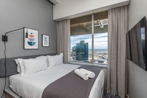 A hotel room with a bed, a large window with curtains, and two framed artworks on the wall.