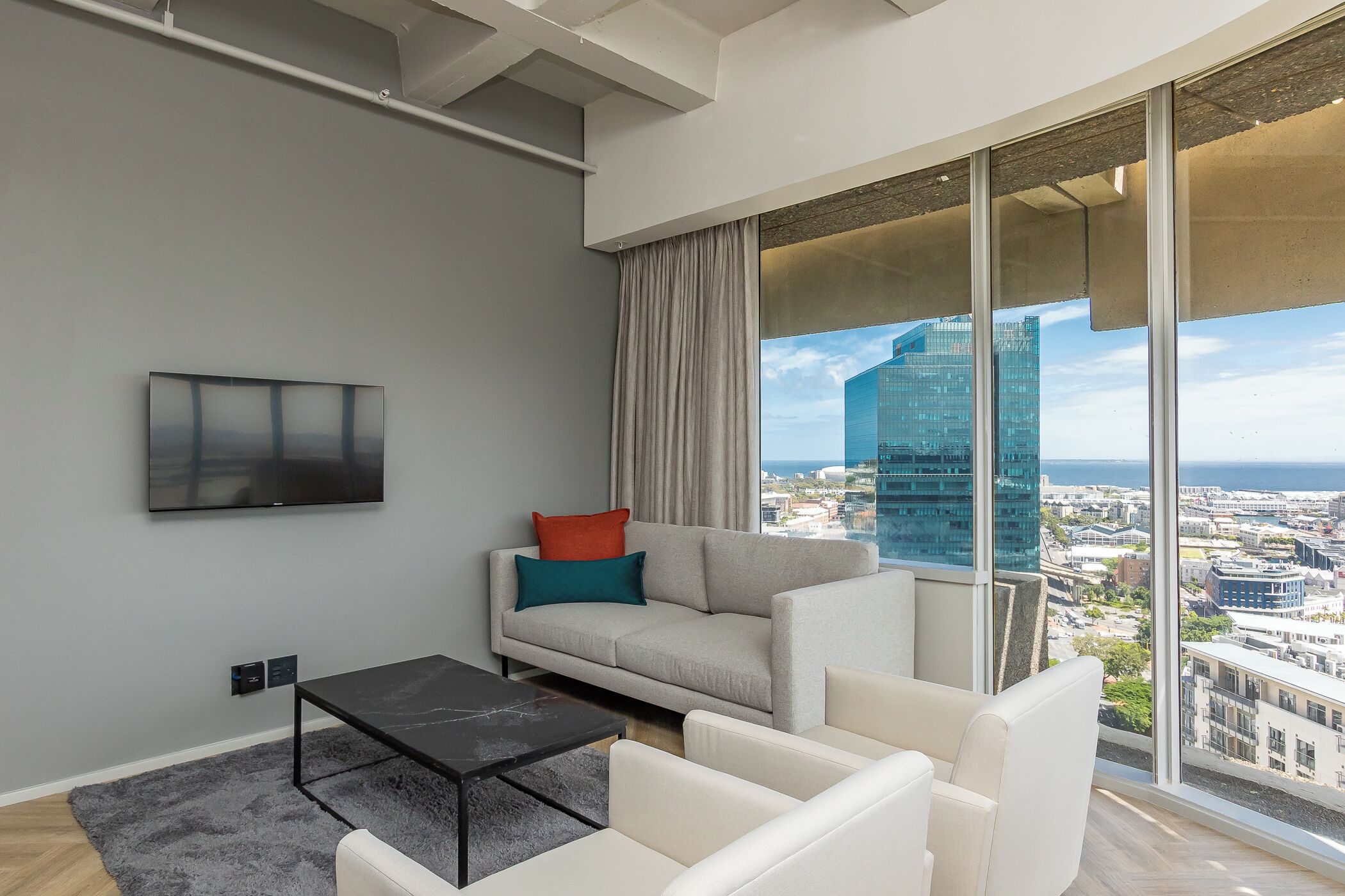 A modern living room with a sofa, a coffee table, and a large window offering a city view.