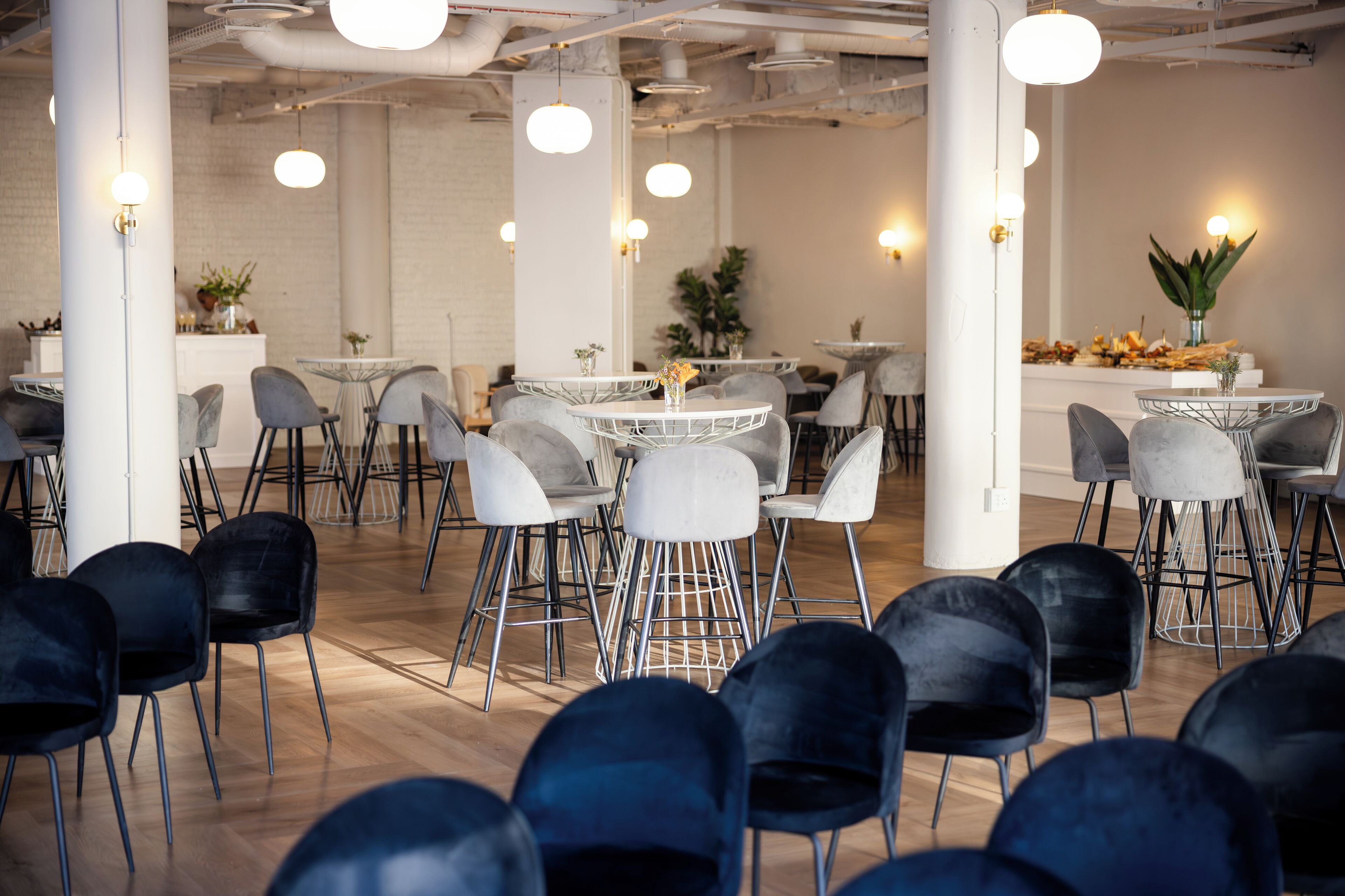 A modern conference room with round tables, grey and black chairs, and pendant lighting.