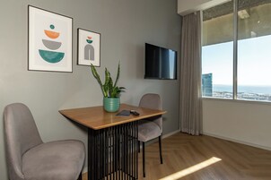 A modern room with a wooden table, two chairs, a potted plant, a framed artwork, and a TV on the wall.