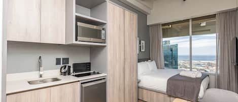 Una habitación de hotel moderna con kitchenette, una cama con vistas y un ventanal grande.
