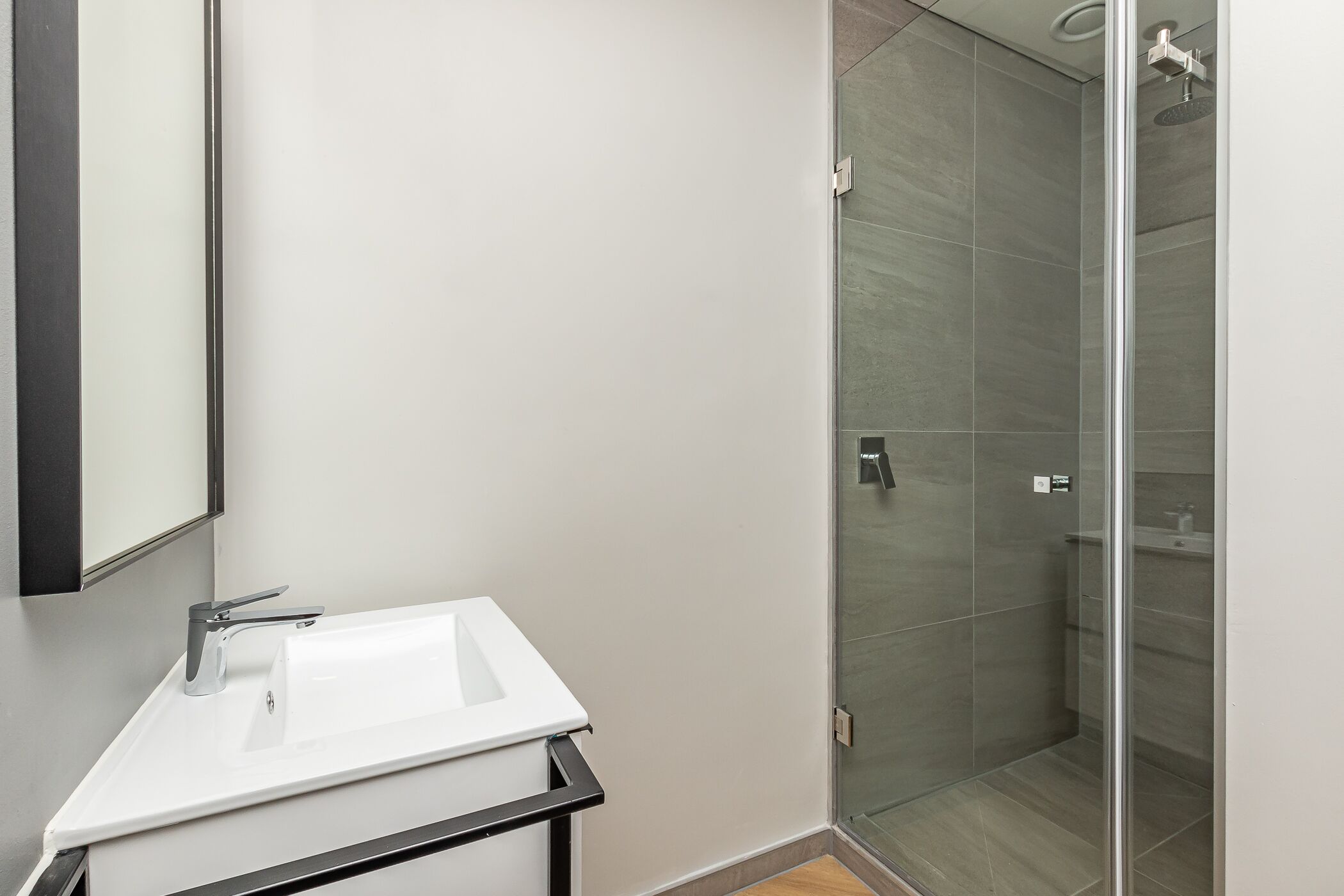 A modern bathroom with a white sink, a glass shower enclosure, and a mirror.
