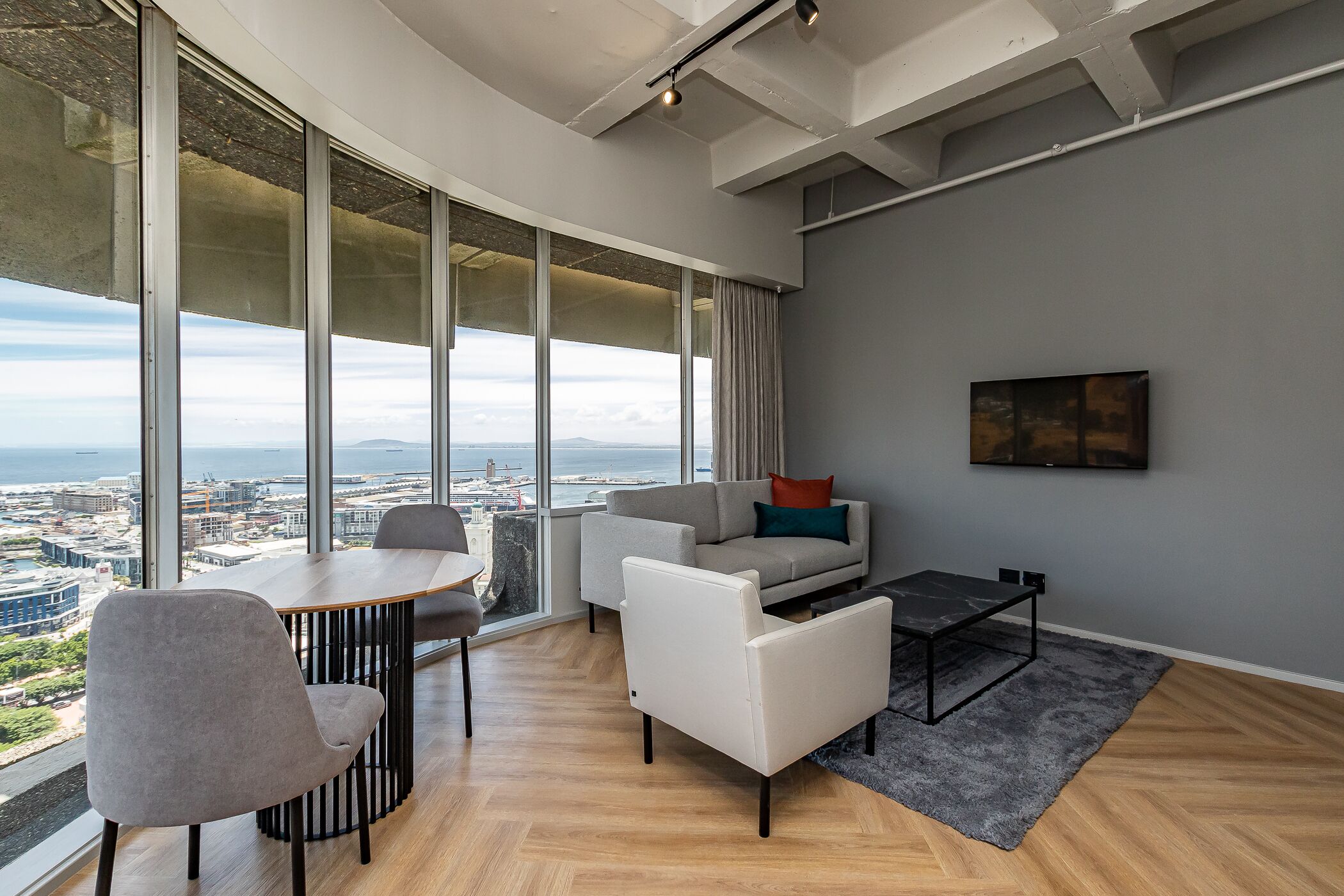 A modern living room with a large window, a sofa, a coffee table, and a dining table.