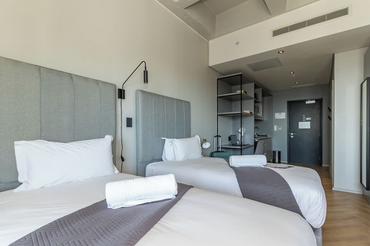 A hotel room with two beds, a desk, a chair, and a wardrobe.