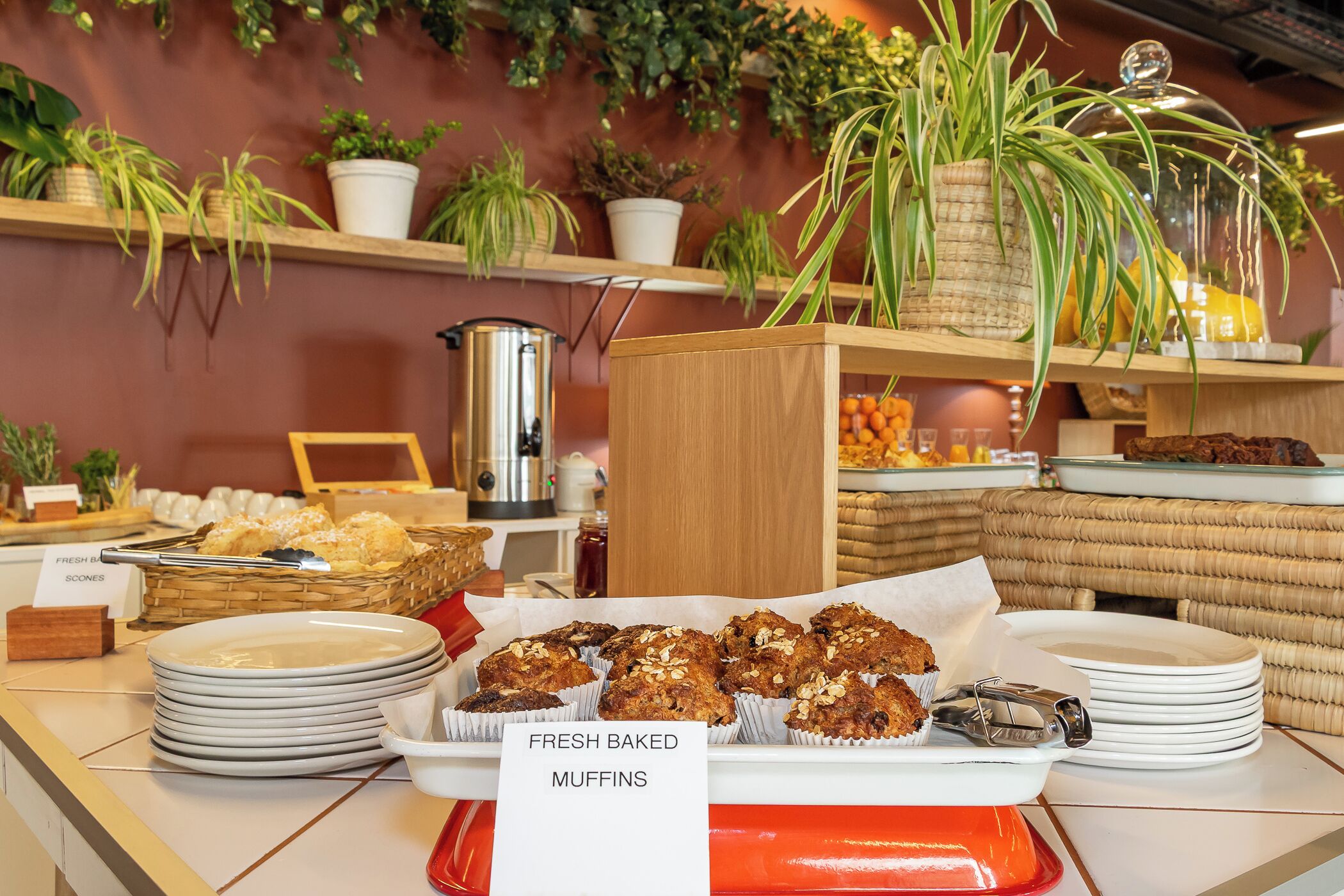 A buffet table with fresh baked muffins and scones, surrounded by plates and a coffee pot.