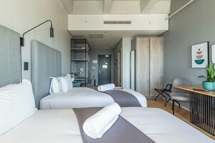 A modern hotel room with two beds, a desk, a chair, and a potted plant.