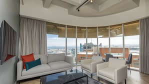 A modern living room with a sofa, armchairs, a coffee table, and large windows offering a city view.