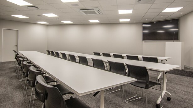 Une salle de conférence équipée d’une longue table, de chaises, d’un tableau blanc et d’un écran de projection.