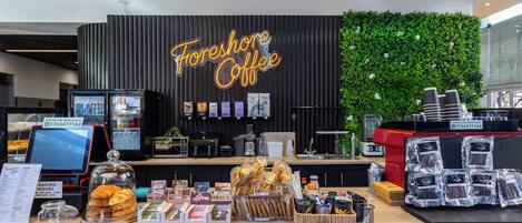 Un comptoir de café avec un panneau néon, un menu numérique et une variété de produits à base de café.