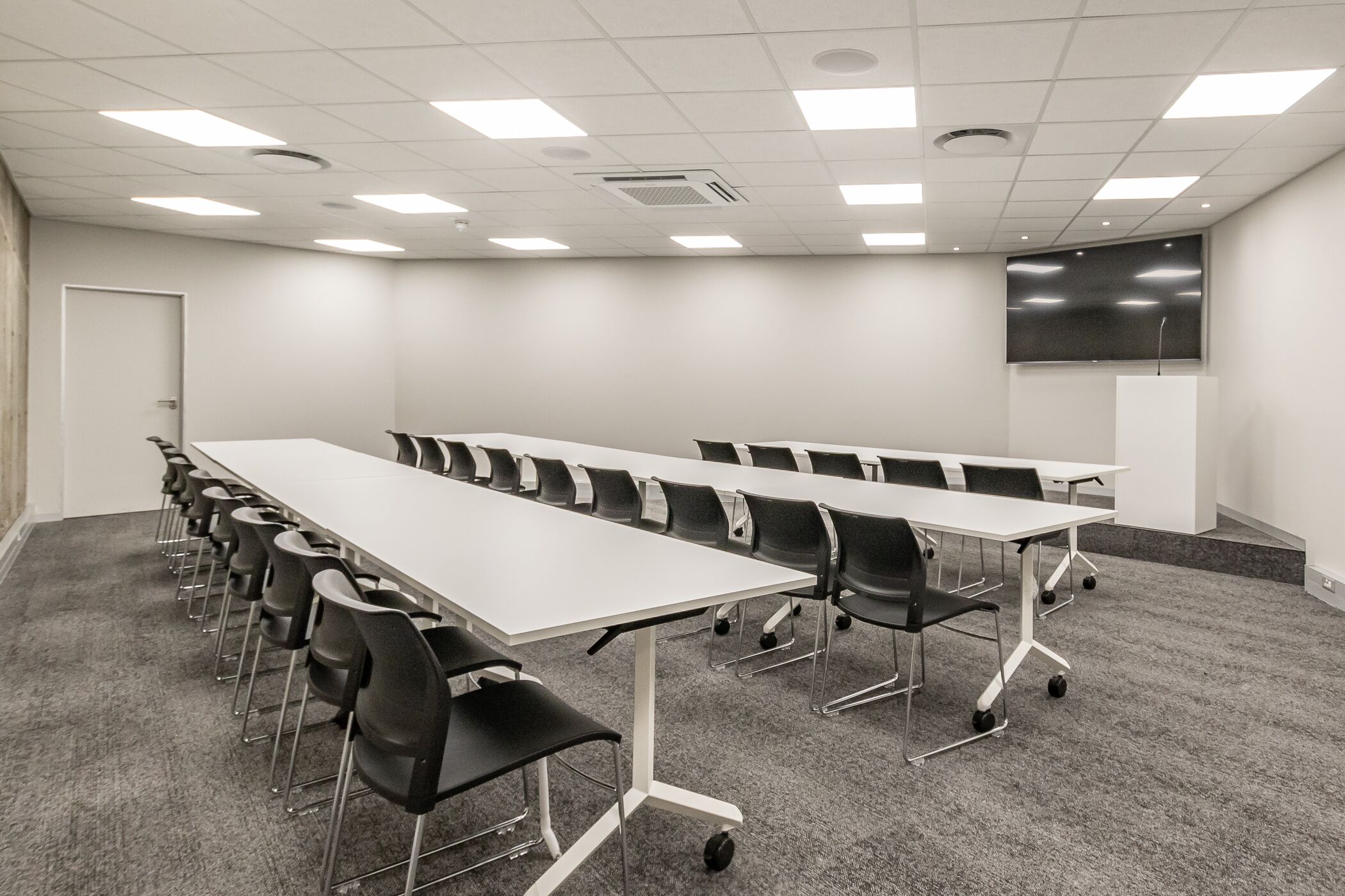 A conference room with a long table, chairs, a whiteboard, a screen, and a door.