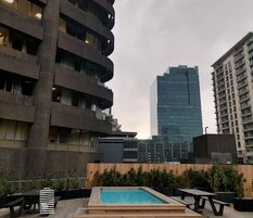 Zona de piscina en la azotea con escalones de madera que bajan a la piscina, rodeada de mobiliario exterior y un paisaje urbano al fondo.