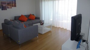 En moderne stue med en grå sofa, orange puder, et hvidt sofabord og et fjernsyn.
