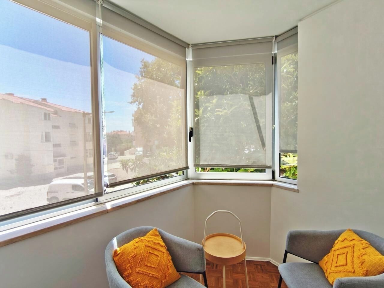 A corner room with two grey chairs, a small wooden table, and a yellow cushion.