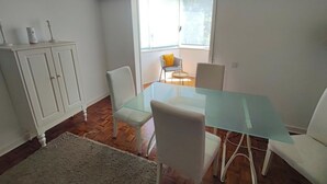 A dining area with a glass table, white chairs, a white cabinet, and a window with a view. - Carcavelos, Cozy 3 bedroom apartment in Cascais (Carcavelos)