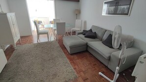 A living room with a sofa, a rug, a fan, and a dining area with chairs and a table. - Carcavelos, Cozy 3 bedroom apartment in Cascais (Carcavelos)