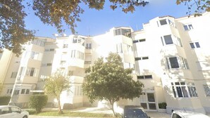A multi-story residential building with balconies, a central courtyard, and a tree in the foreground. - Carcavelos, Cozy 3 bedroom apartment in Cascais (Carcavelos)