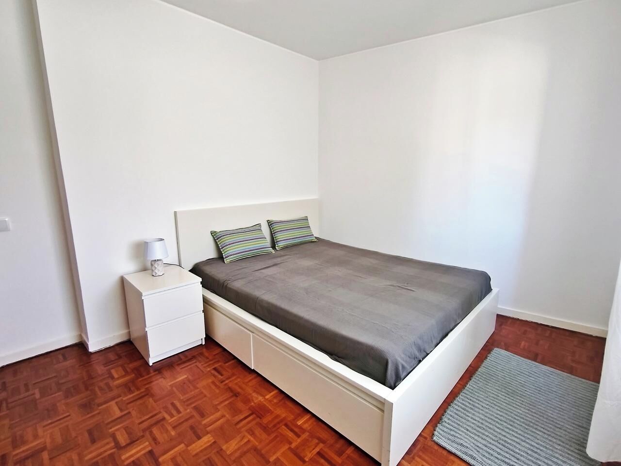 Un dormitorio con cama, mesita de noche y suelo de madera.