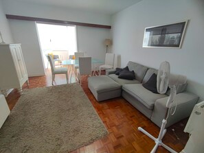 A living room with a sofa, a fan, a rug, and a dining area with chairs and a table.