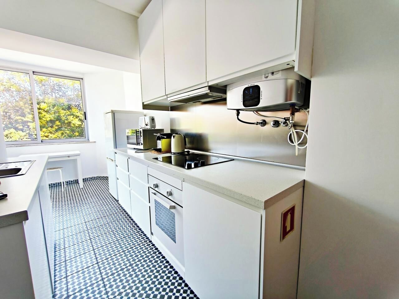 Una cocina moderna con armarios blancos, horno empotrado y ventana con vistas a la vegetación.