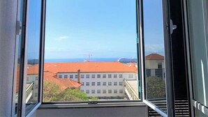 A view from a window with a clear sky, a building with a red roof, and a distant structure with a red tower. - Madeira, 3 bedroom apartment w Ocean Views Funchal (Funchal)